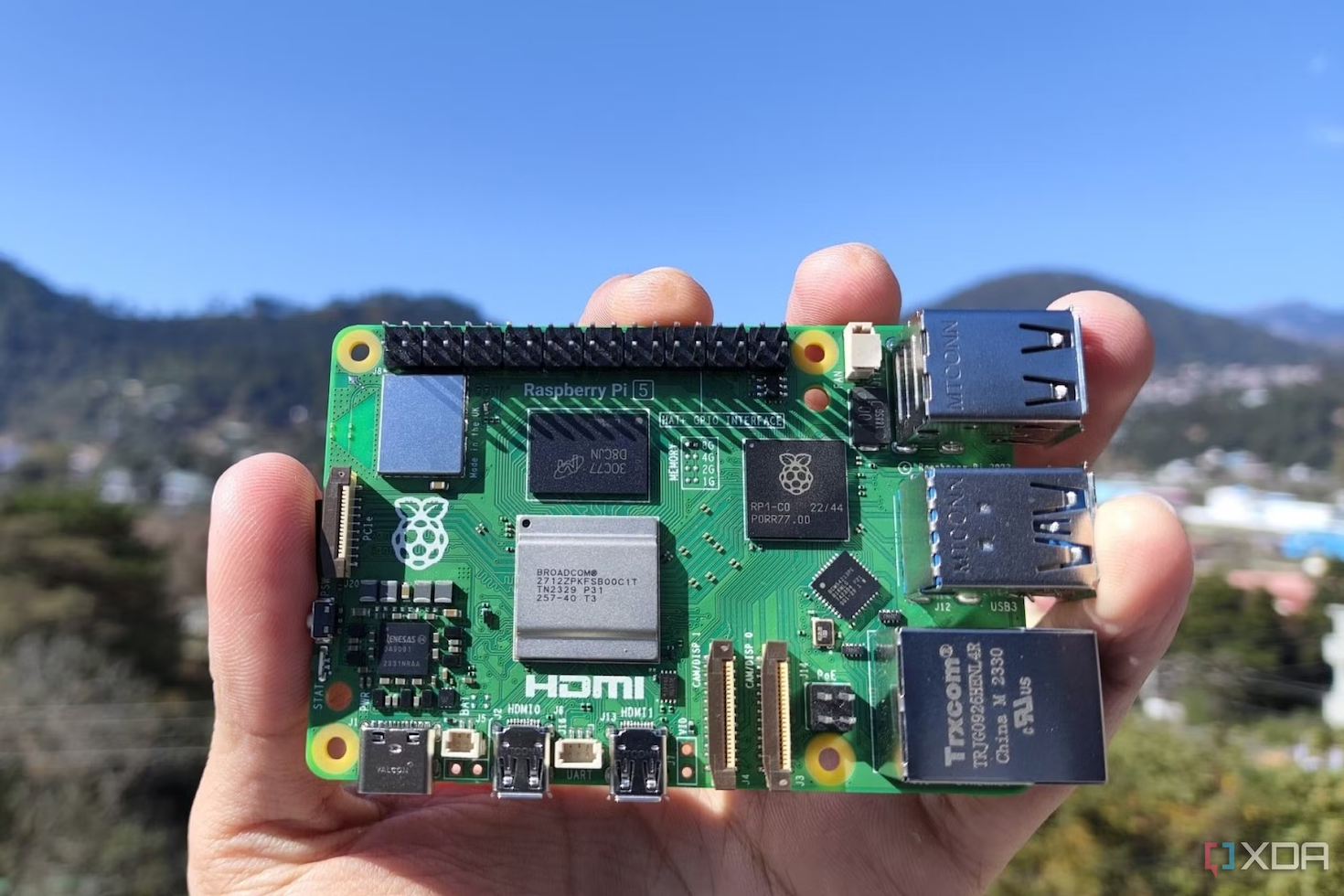 A raspberry pi 5 held in front of a gorgeous landscape. It fits in the palm of a hand