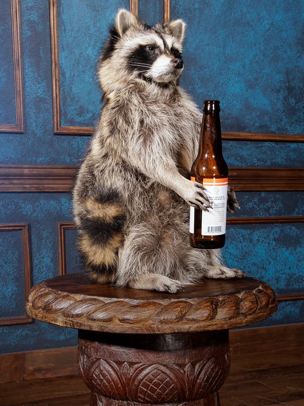 A statue of a raccoon drinking a bottle of beer